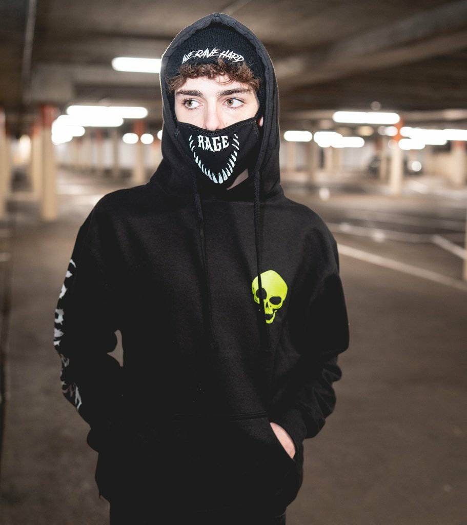 A person wearing a black hoodie with a text and logo on the front and a green skull design on the back, in a parking garage setting.